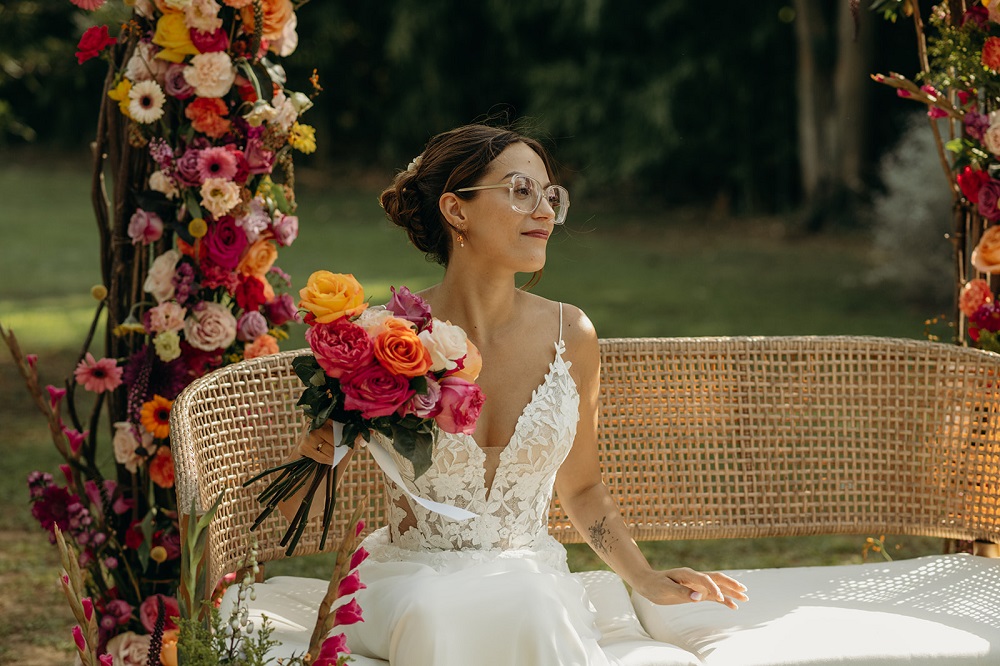 Mariée assise sur une banquette qui tient son bouquet de roses