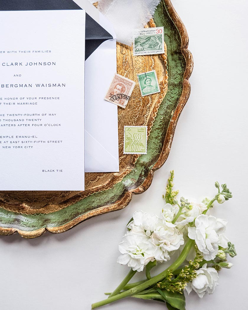 Faire-part de mariage artisanal posé sur une table en marbre blanc avec une branche d'eucalyptus et une enveloppe